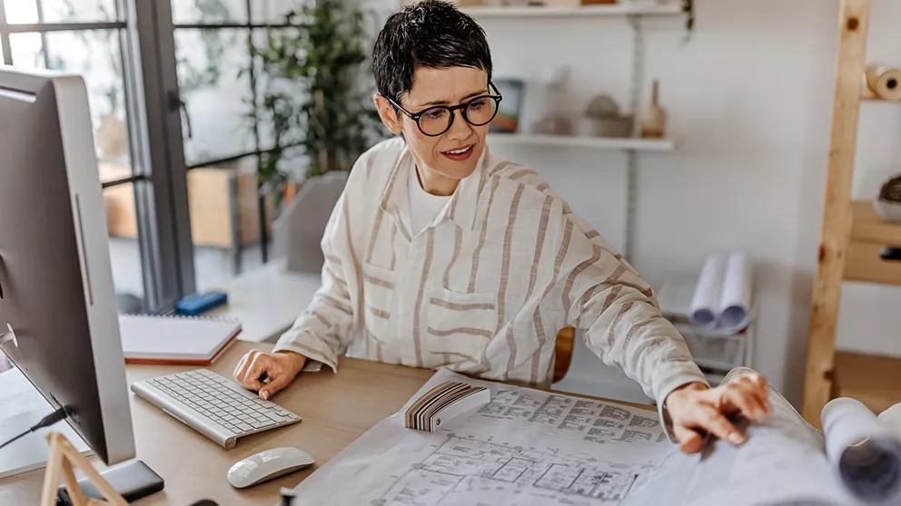 Mujer con camisa blanca trabajando detrás de un escritorio y con gafas de montura negra.