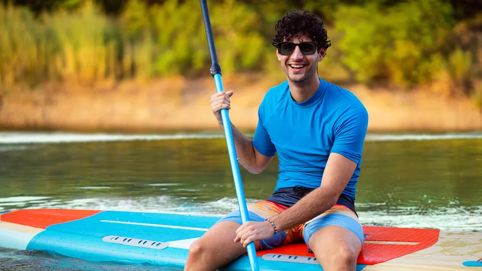 Chico riendo en una tabla de SUP con gafas de sol polarizadas HOYA
